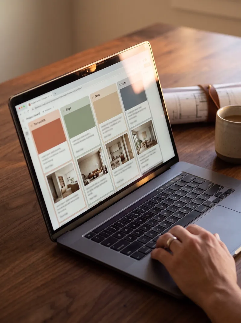 Notebook com quadro de projetos em colunas coloridas, rolo de planta e café na mesa